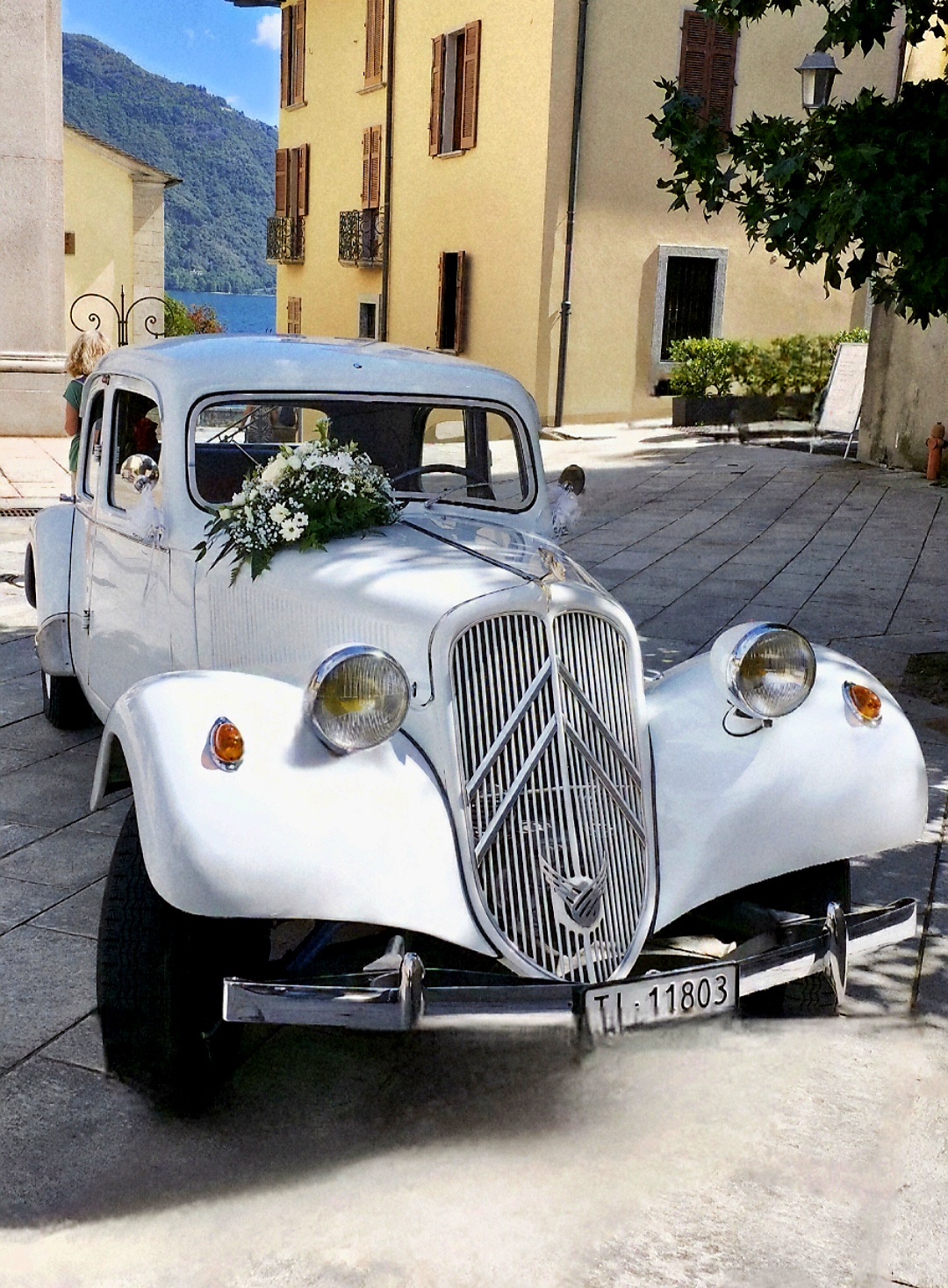 La Traction Avant addobbata di fiori bianchi nella piazza del borgo, sul lago